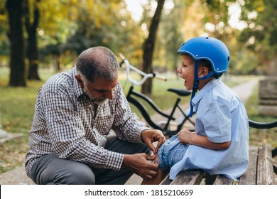 Grandfather Puts Band Aid On Knee To His Grandson