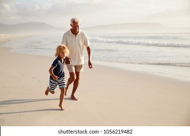 Grandfather Running Along Beach With Grandson On Summer Vacation