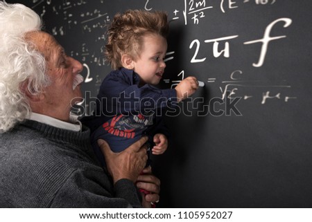 Grandfather scientist with grandchild in arm writing at the blackboard