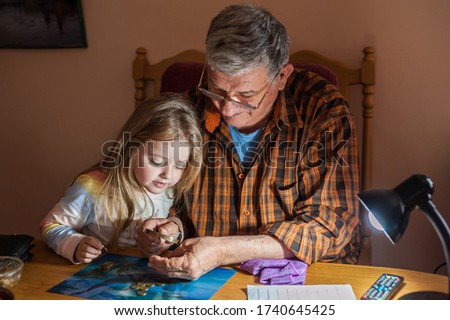 Grandfather shows coins to a small beautiful granddaughter through a magnifier. The concept of common interests and family unity. Family values.