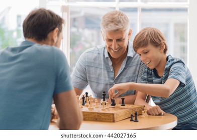 Grandfather Teaching Grandson How To Play Chess. Father And Son Playing Chess With Grandchild. Grandfather Watching Son And Grandson Playing Board Game At Home.