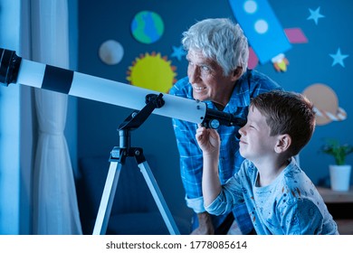 Grandfather Teaching Grandson Using Telescope To See Planets And Galaxy. Child Watching Stars Through A Telescope At Night With Senior Man. Grandpa And Grandchild Looking Together At Positive Future.