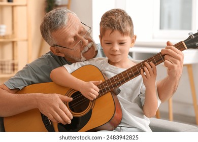 Grandfather teaching his cute little grandson playing guitar at home - Powered by Shutterstock