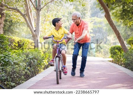 Grandfather trying to teach grandson to ride a cycle at park.