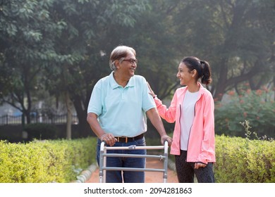 Grandfather Using Mobility Walker At Park While Having Fun With Granddaughter.
