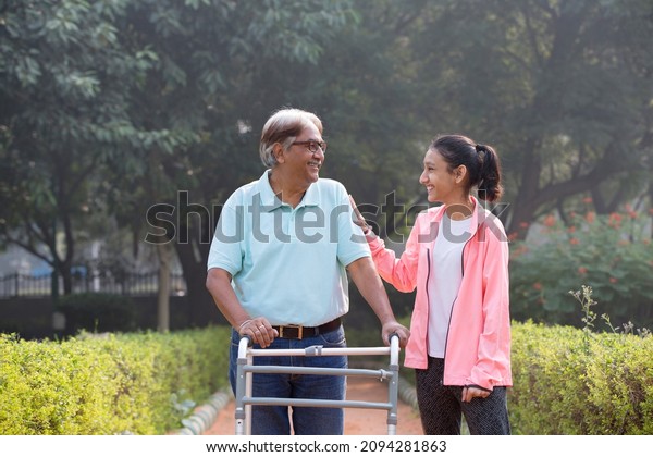 Grandfather using mobility walker at\
park while having fun with\
granddaughter.\
