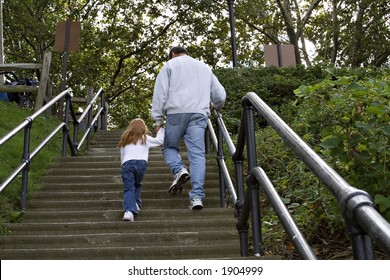 Grandfather Walking Child Up Concrete Stairs At A Park.