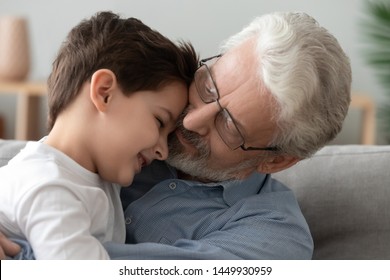 Grandfather Wearing Glasses Hugging Little Grandson, Expressing Love And Support Close Up, Caring Granddad And Preschool  Grandchild Boy Sitting On Couch Together, Good Family Relationship