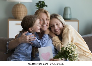 Grandma embrace little granddaughter, thank adult daughter for gift on birthday, holding spring chamomile flowers and postcard, smiling feel happy. Live events, Mothers Day and 8-march celebrations - Shutterstock ID 2225721037
