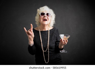 Grandma with glasses and drink in hand showing rock sign  - Shutterstock ID 585619955