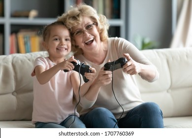 Grandma Granddaughter Enjoy Videogames Sit On Couch At Home, Younger Older Relatives, Funny People Holding Playing Looking At Pc Or Tv Screen, Weekend Activity With Kids Concept