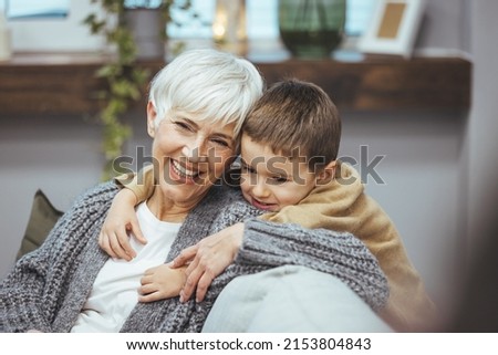 Grandma and grandson spend beautiful time together, they are happy and enjoy themselves. The child hugs her with a lot of love. Happy grandmother with her grandson in the house.