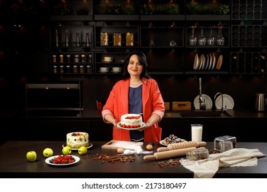 Grandma Is Holding A Fruit Pie In A Black Kitchen. Cooking Homemade Cakes. Cake. Cookie. Bakery Products. Eggs. Flour. Milk. Apples