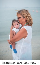 Grandma Holding Newborn Baby Boy At The Beach By The Seaside On The Summer Vacation