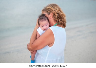 Grandma Holding Newborn Baby Boy At The Beach By The Seaside On The Summer Vacation