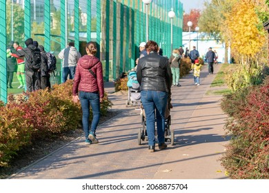 Grandma And Mom With A Baby Carriage Walk Near The Football Stadium With The Townspeople On An Autumn Day 