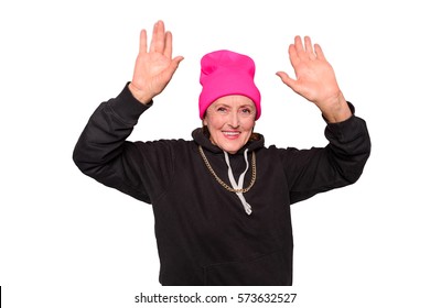 Grandma Puts Her Hands Up. Modern Clothes Like A Pink Hat And A Black Hoodie With A Chain On Is What Makes This Granny Look Absolutely Crazy. Horizontal Photo Of Old Gangsta Woman Isolated On White.