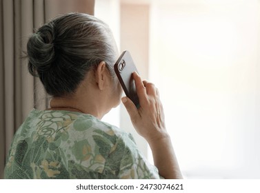 Grandma standing nearby the window and talking to family on the phone at bedroom in the morning. Back view, copy space. - Powered by Shutterstock