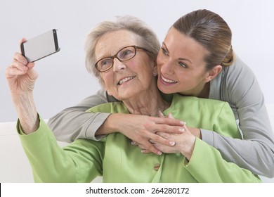 Grand-Mother and attractive young grand-daughter photographing themselves by mobile phone, smiling happily.