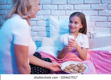 Grandmother Brings Granddaughter Cookies And Milk In Bed At Night At Home.