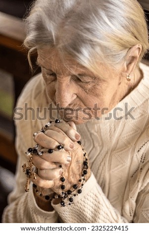 grandmother with clasped hands holding the rosary and praying with great faith