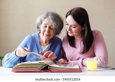 Grandmother and daughter watching a family album with old photos together - Linking generations in a common activity - An elderly and a young woman talking together-Family relations concept - Powered by Shutterstock