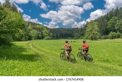 Grandmother with electric mountain bike and granddaughhter without electric help on a smooth meadow trail in the Franconian Switzerland area of Bavaria, Gemany