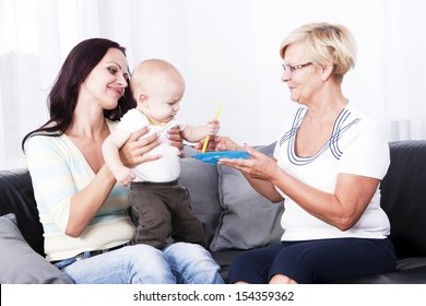 A Grandmother Feeding The Baby With The Mother.