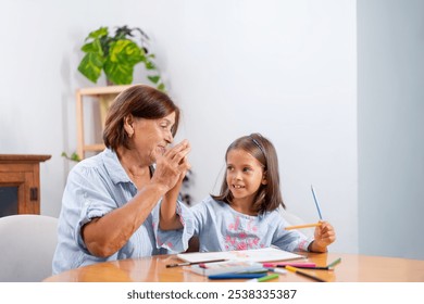 Grandmother gives high five to granddaughter, who is excitedly holding colored pencil, celebrating creativity and joy in their cozy home  - Powered by Shutterstock