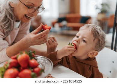Grandmother giving homegrown strawberries to her little grandson.