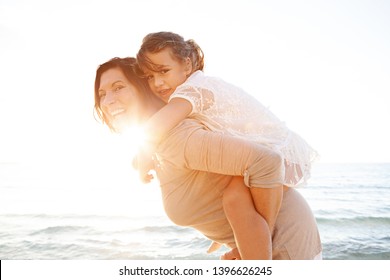 Grandmother And Grand Daughter Enjoying Sunny Beach Holiday Together Joyful Smiling With Sun Flare Sunset Sky, Outdoors Space. Senior And Child Fun Bonding Family Travel Activities, Leisure Lifestyle.