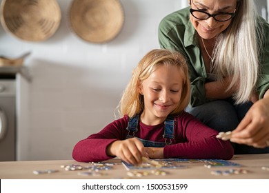 Grandmother and granddaughter doing puzzle together at home. Senior woman helping smiling little girl to solve puzzles. Happy grandchild solving puzzle at home while mature granny, playing together.