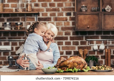 grandmother and granddaughter embracing on kitchen and looking at freshly prepared turkey for thanksgiving dinner