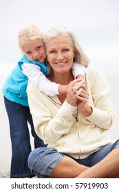 Grandmother And Granddaughter On Holiday Sitting On Winter Beach