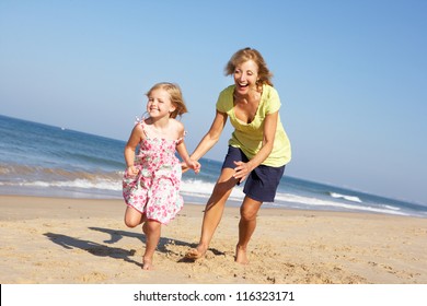 Grandmother And Granddaughter Running Along Beach