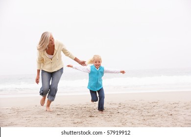 Grandmother And Granddaughter Running Along Winter Beach