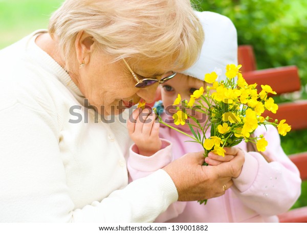 Grandmother with granddaughter sniffing yellow\
flowers in the park