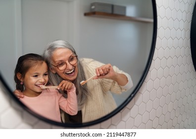 Grandmother with granddaughter standing indoors in bathroom, brusing teeth and looking at mirror. - Powered by Shutterstock