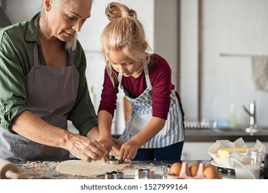 Grandmother And Granddaughter Using Cookie Cutter To Cut Dough In Shapes. Little Cute Girl And Senior Grandma In Apron Preparing Cookies For Christmas. Grandchild With Old Granny Cooking In Kitchen.
