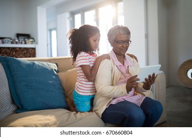 Grandmother and granddaughter using digital tablet on sofa in living room at home - Powered by Shutterstock