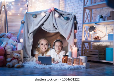 Grandmother And Granddaughter Are Watching Movie On Tablet In Cozy Blanket House At Night At Home.