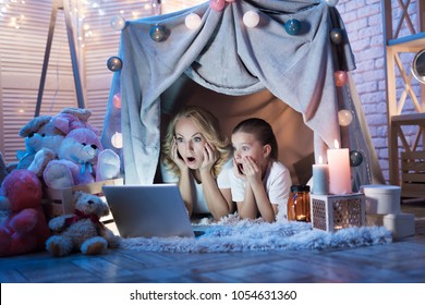 Grandmother and granddaughter are watching movie on laptop in cozy blanket house at night at home.