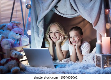 Grandmother And Granddaughter Are Watching Movie On Laptop In Cozy Blanket House At Night At Home.