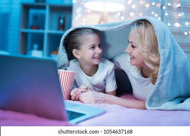 Grandmother And Granddaughter Are Watching Movie On Laptop Under Blanket On Bed At Night At Home.