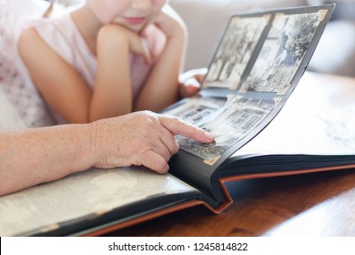 Grandmother And Granddaughter Watching Old Photo Album At Home. Senior Woman Shows Child Black And White Photos. Hands Of Retired Person And Kid. Family Leisure.