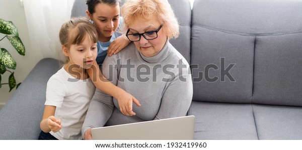 Grandmother with\
granddaughters use a\
computer