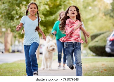 Grandmother And Granddaughters Walking Dog Along Suburban Street