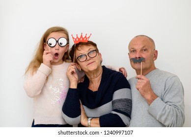 Grandmother and Grandfather with paper mask having fun with grandchild . Happy family celebrating new year, birthday , christmas, purim. Old funny grandpa with fake mustache, grandma with crown. - Powered by Shutterstock