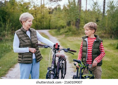 Grandmother And Grandson On Bikes Outdoors Smiling And Talking. Different Generation Family Communication Concept.