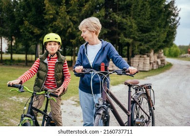 Grandmother And Grandson On Bikes Outdoors Smiling And Talking. Different Generation Family Communication Concept.